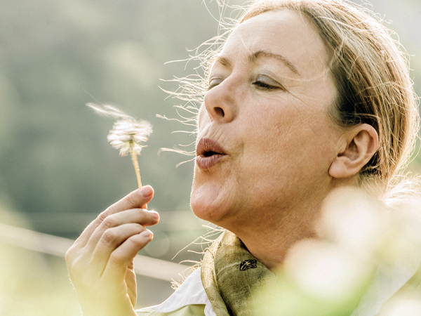 Mature woman blowing dandelion flower Psychotherapie Taruna N. Reupsch